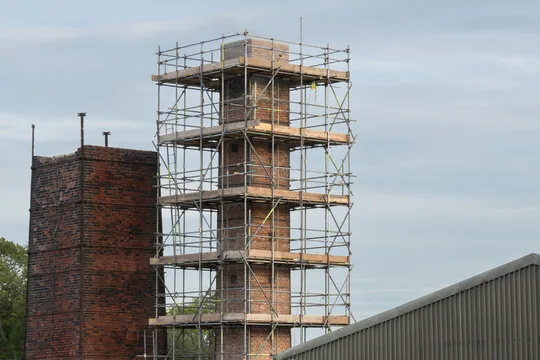 Scaffolding built around a tall brick chimney so it can be worked on safely, next to another chimney
